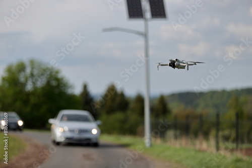 Dron w locie, w powietrzu, w tle panele słoneczne z latarnią uliczną, samochody osobowe na drodze.