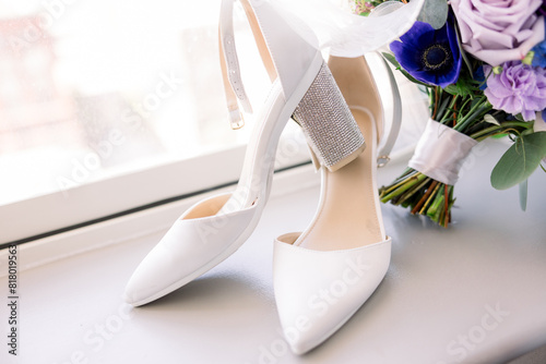 White wedding shoes styled on a window ledge next to the bridal bouquet. 