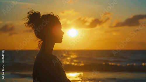 A silhouette of woman to be gazing at the horizon as the sky transitions into shades of orange. clouds