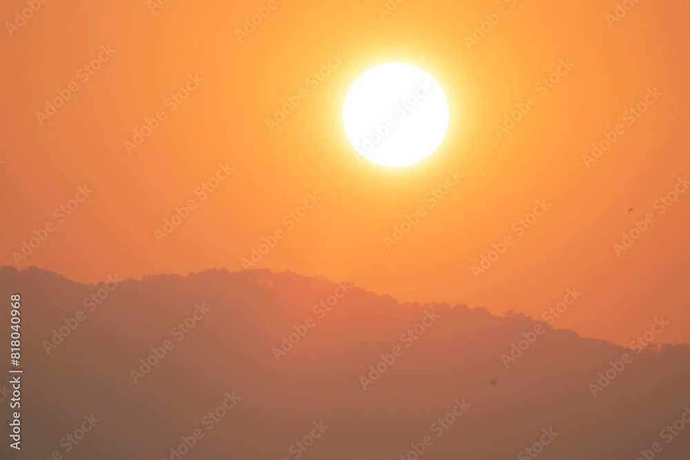 A large sun is in the sky, with a mountain range in the background