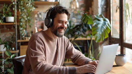 Young smiling man in headphones typing on laptop keyboard while sitting by workplace and taking part in online webinar or lesson 