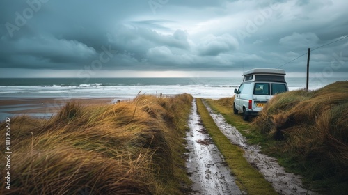Camper van facing a stormy beach, wet sandy path winding through grass, heavy rain and dark clouds looming, peaceful solitude