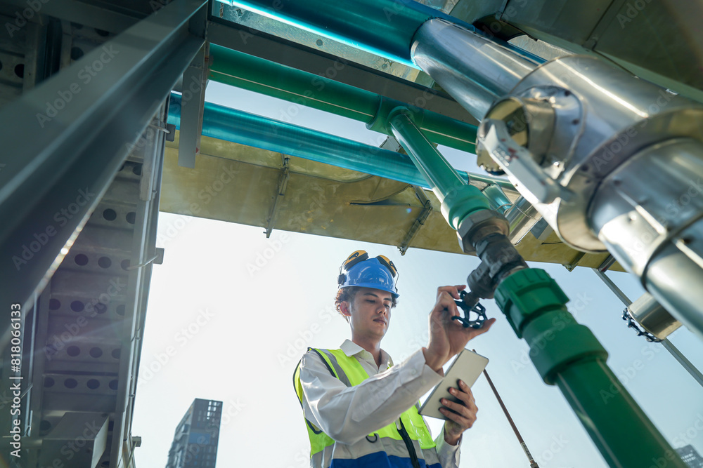 Male engineer monitoring machinery on a rooftop with city skyline in the background, wearing safety gear Male engineer monitoring machinery on a rooftop with city skyline in the background, wearing safety gear