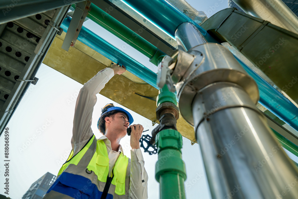 Male engineer monitoring machinery on a rooftop with city skyline in the background, wearing safety gear Male engineer monitoring machinery on a rooftop with city skyline in the background, wearing safety gear