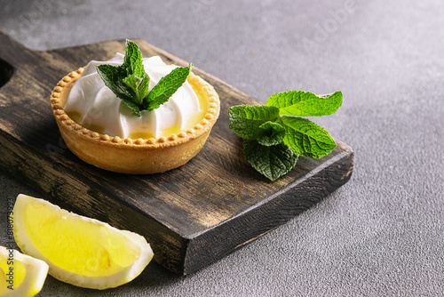 Aromatic homemade lemon tart with fresh mint leaves on dark stone background close up.