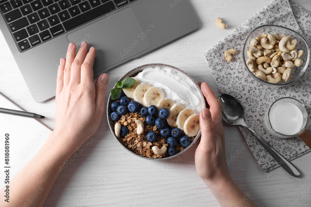 Φωτογραφία Woman with bowl of tasty granola working with laptop at white wooden table, top