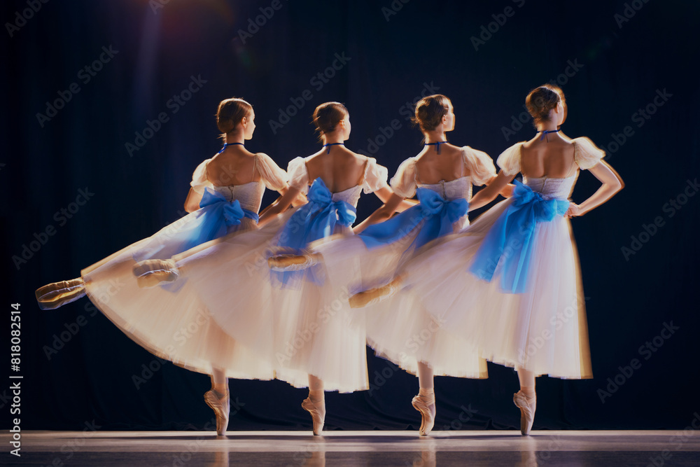 Φωτογραφία Rear view of young girls, ballet dancers in white tutus with blue bows on pointe dancing in motion on stage