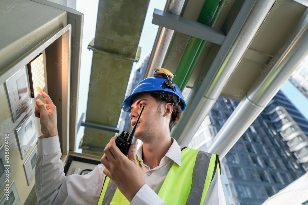 Industrial engineer adjusting pipeline valve with radio communication on construction site. Engineer on urban construction site using radio to coordinate with team on a sunny industrial rooftop. Industrial engineer adjusting pipeline valve with radio communication on construction site. Engineer on urban construction site using radio to coordinate with team on a sunny industrial rooftop.