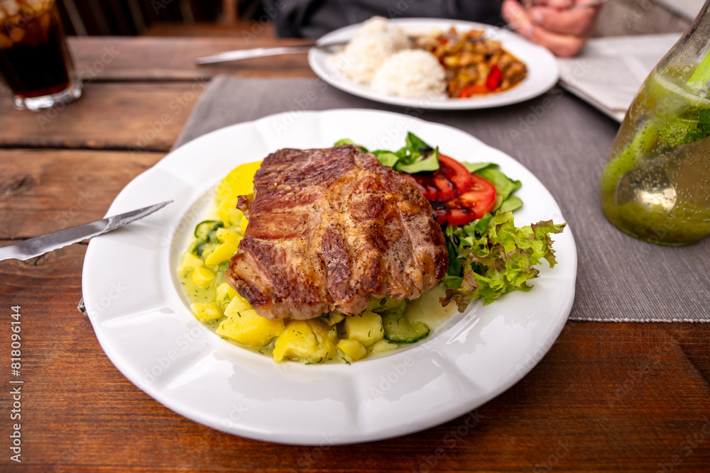 Juicy pork steak with light potato salad and vegetable in first plate, rice, second meal on table. Juicy pork steak with light potato salad and vegetable in first plate, rice, second meal on table.