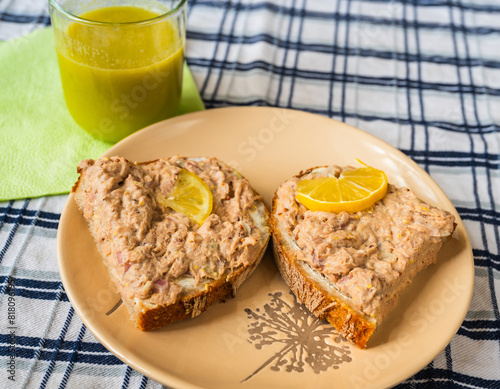 2 slice bread with tuna fish spread, lemon, green smoothie in glass on table.
