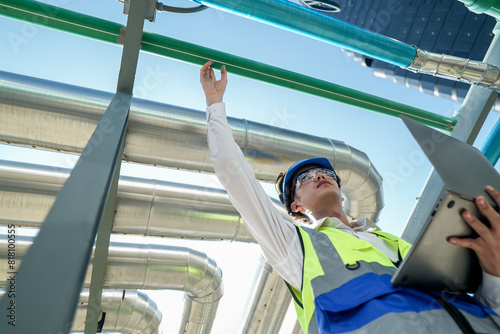 Industrial engineer adjusting pipeline valve with radio communication on construction site. Engineer on urban construction site using radio to coordinate with team on a sunny industrial rooftop.