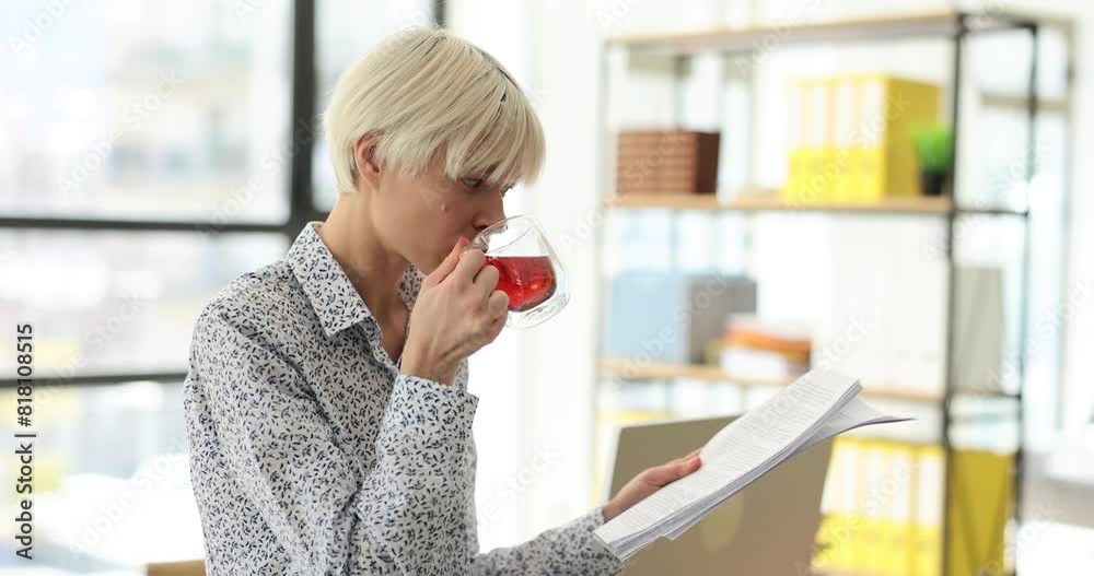 Employee reads business report and holds tea cup standing in light office. Business lady prepares for corporate meeting during work break slow motion Employee reads business report and holds tea cup standing in light office. Business lady prepares for corporate meeting during work break slow motion