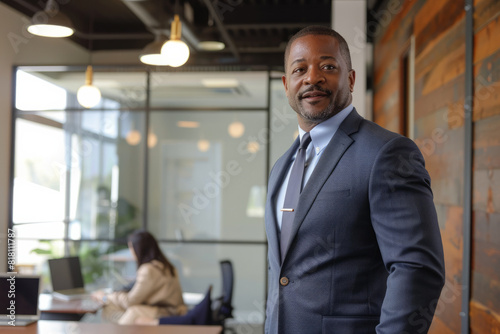 A confident African American businessman, standing tall in a modern office space, leading a team meeting with charisma and authority, his sharp suit and commanding presence exuding professionalism. © AI_images