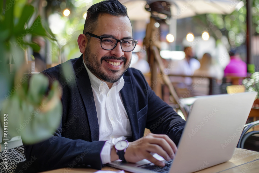 A Hispanic businessman works remotely from a cafe, typing on his laptop with a smile. Dressed in a suit and glasses, he exudes success and determination while seated at a wooden desk on a sunny day. A Hispanic businessman works remotely from a cafe, typing on his laptop with a smile. Dressed in a suit and glasses, he exudes success and determination while seated at a wooden desk on a sunny day.