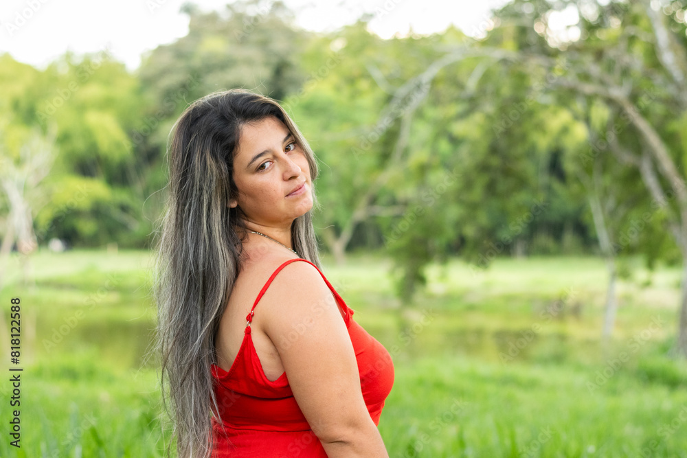 latina woman walking through a field surrounded by green nature, looking backwards latina woman walking through a field surrounded by green nature, looking backwards