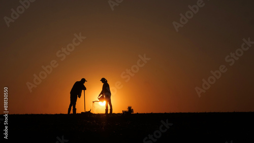 A couple of farmers plant seedlings in a field at sunset. A man digs  a woman waters