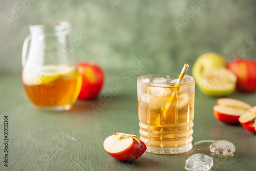 Apple juice and sparkling water in glass. Apfelschorle German drink. Apple fruit, ice and leaves in background. Summertime cold drink