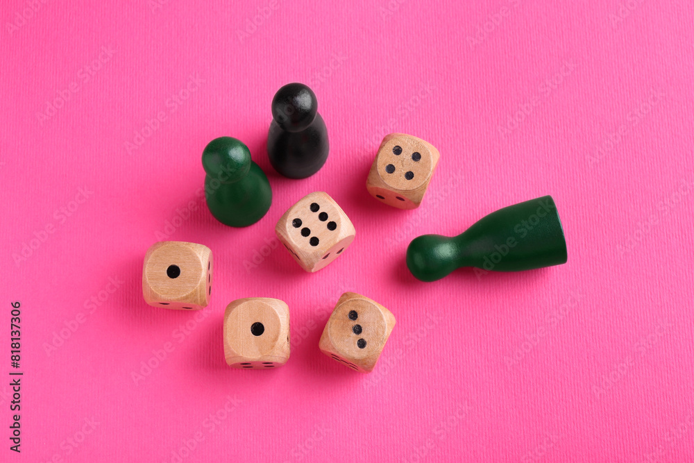 Wooden dices and color game pieces on pink background, flat lay Wooden dices and color game pieces on pink background, flat lay