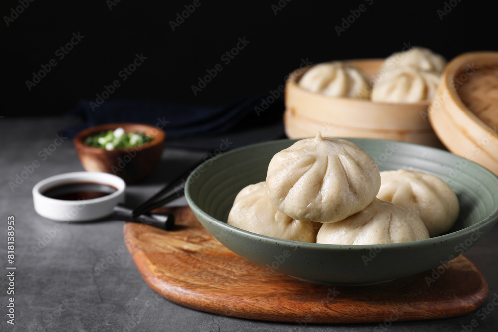 Delicious bao buns (baozi) in bowl on grey textured table, closeup