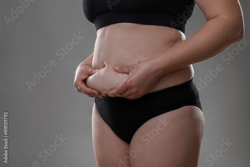 Woman touching belly fat on grey background, closeup. Overweight problem © New Africa
