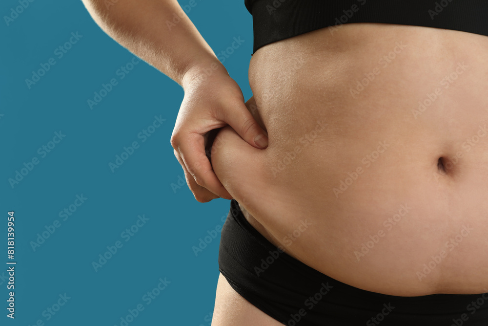 Fototapeta premium Woman touching belly fat on light blue background, closeup. Overweight problem