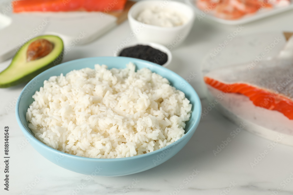 Cooked rice in bowl and other ingredients for sushi on white marble table, closeup Cooked rice in bowl and other ingredients for sushi on white marble table, closeup