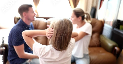 Teen girl covers ears with hands to avoid listening to argument of parents. Man and woman sit on sofa quarreling in presence of daughter slow motion photo