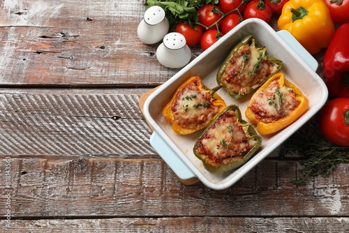 Tasty stuffed peppers in dish and ingredients on wooden table, flat lay. Space for text
