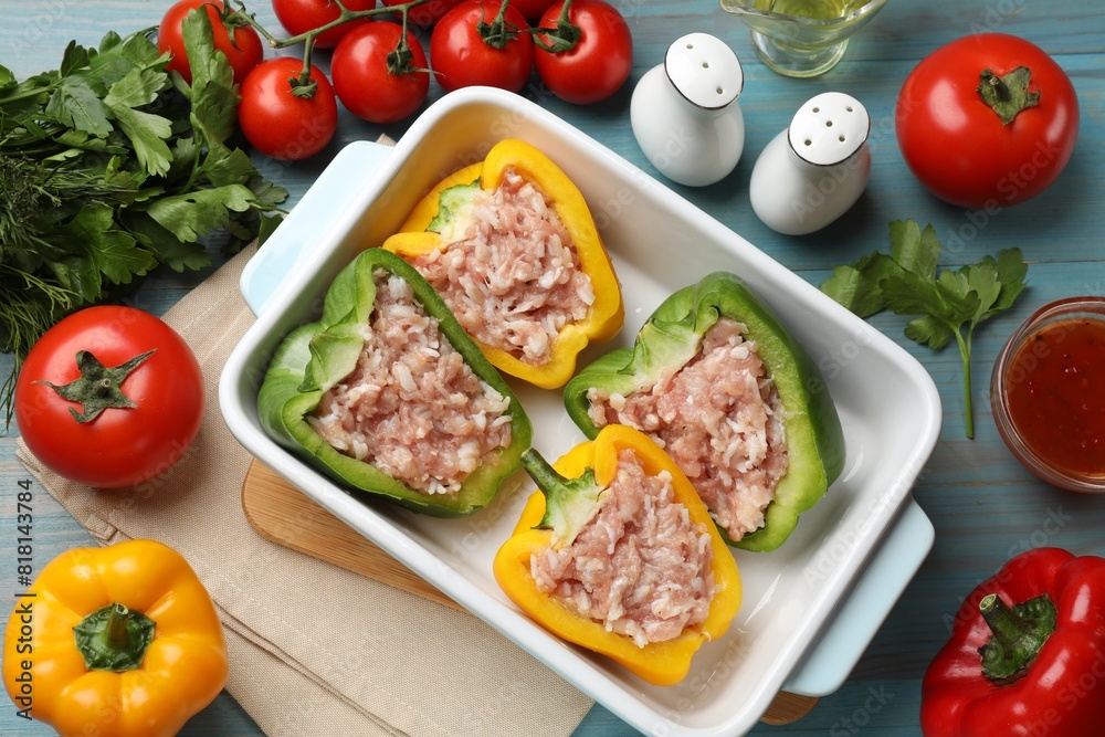 Raw stuffed peppers in dish and ingredients on wooden table, flat lay