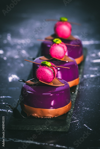 Three tartlets with purple creamy glaze, decorated with macaraon, chocolate and pistachio