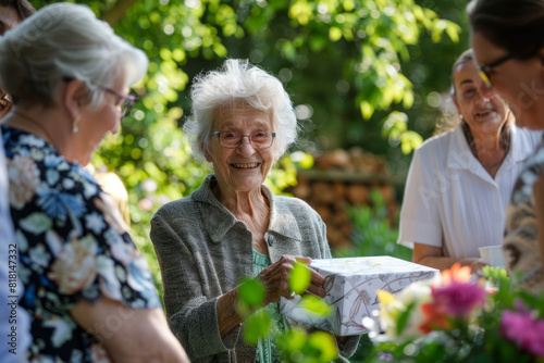 Family gathering in the garden to celebrate the birthday of a senior lady, who is delightedly receiving a gift. photo