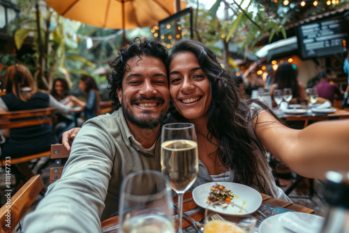Latino couple having a date at a restaurant  taking a selfie on the terrace. The boyfriend and girlfriend delighting in the springtime atmosphere as they dine outdoors.