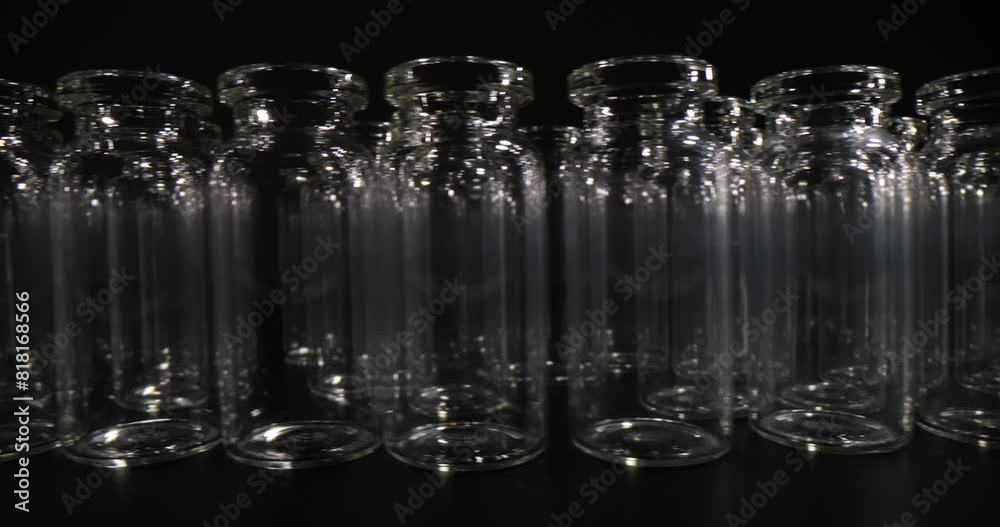 Transparent glass vials for vaccines standing in long row on dark table. Glassware for laboratory and medical purposes on black background Transparent glass vials for vaccines standing in long row on dark table. Glassware for laboratory and medical purposes on black background