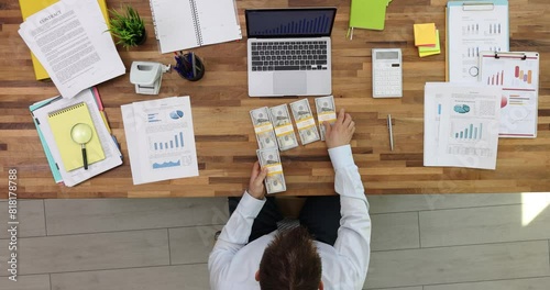 Businessperson puts dollar packs by laptop on table. Entrepreneur counts cash profit in corporate office. Money income after good deal upper view photo