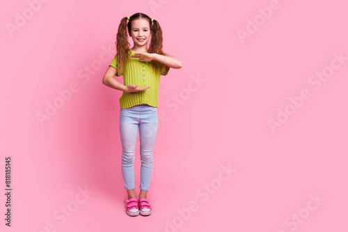 Full body photo of cute little girl hold empty space show measure dressed stylish green clothes isolated on pink color background