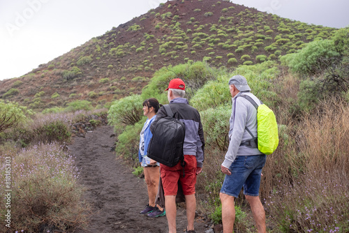 Rear view of active caucasian group of senior friends walking in the nature of Malpais de Guimar in Tenerife island with backpack on shoulders. Healthy lifestyle for retired men and woman photo