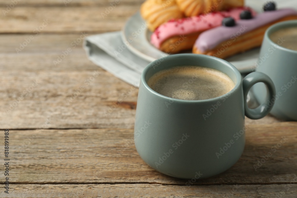 Aromatic coffee in cups, tasty eclairs and profiteroles on wooden table, space for text Aromatic coffee in cups, tasty eclairs and profiteroles on wooden table, space for text