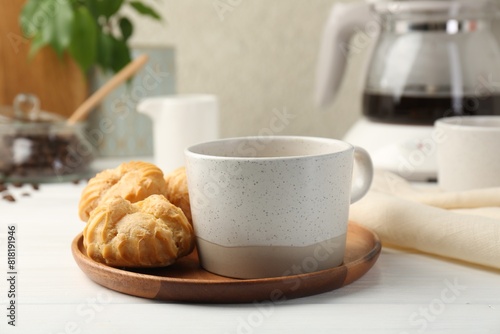 Cup of drink and tasty profiteroles on white wooden table