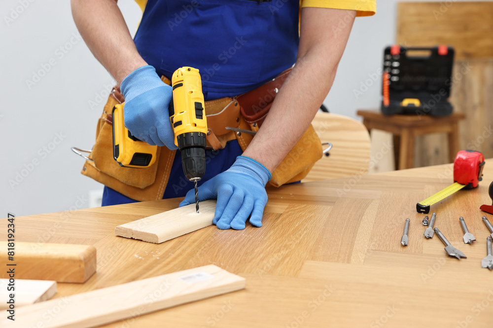 Young worker using electric drill at table in workshop, closeup Young worker using electric drill at table in workshop, closeup