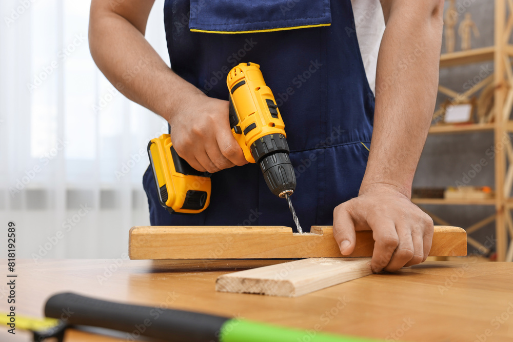 Young worker using electric drill at table in workshop, closeup Young worker using electric drill at table in workshop, closeup