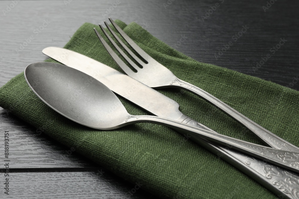 Stylish setting with cutlery and napkin on black wooden table, closeup
