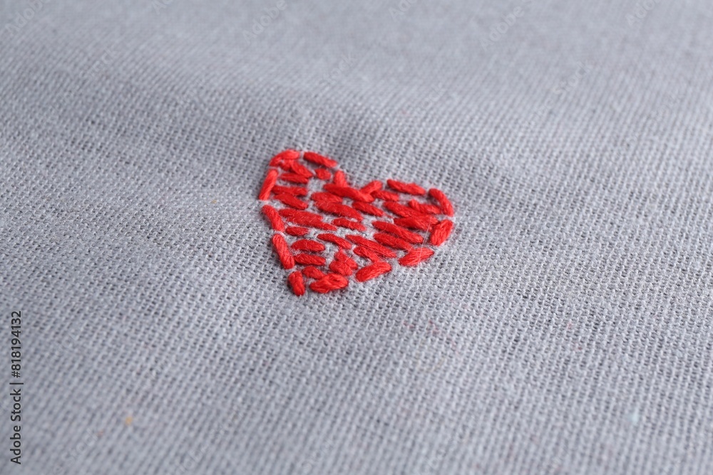 Fototapeta premium Embroidered red heart on gray cloth, closeup
