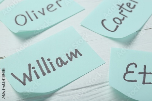 Paper stickers with different names on white wooden table, closeup. Choosing baby's name