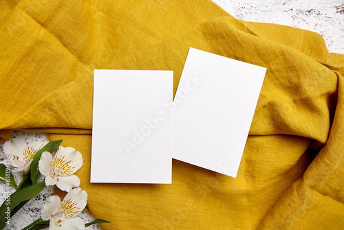 Two blank invitation cards on a rich golden textile background, accompanied by white alstroemeria flowers © mikeosphoto
