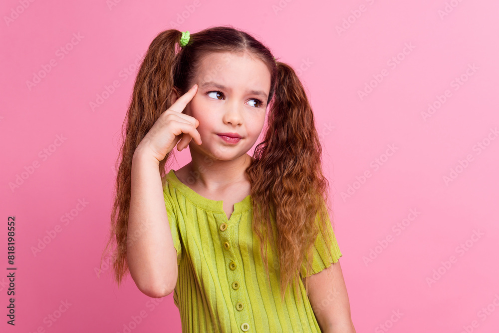 Photo portrait of lovely little girl touch temple look minded empty space dressed stylish green garment isolated on pink color background Photo portrait of lovely little girl touch temple look minded empty space dressed stylish green garment isolated on pink color background