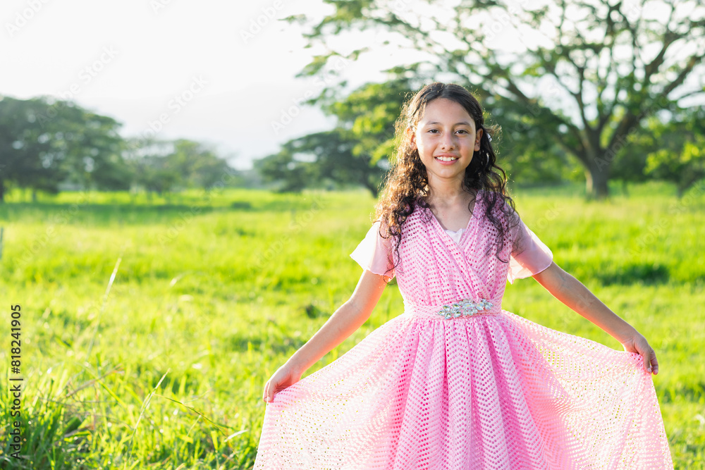 little brunette latina girl in pink dress clutching her dress with her hands, green field with sunset little brunette latina girl in pink dress clutching her dress with her hands, green field with sunset