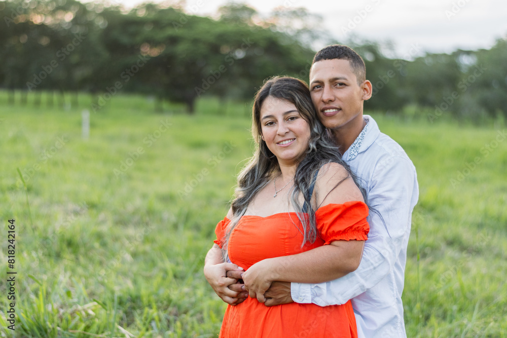 young latin couple, man hugging his girlfriend from behind while looking and smiling, interracial couple