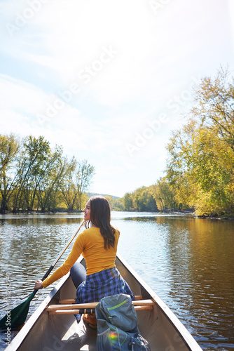 Woman, back and canoeing paddle in forest on lake, wellness hobby and backpack for supplies and rowing for water sport. Vacation, relax and explore exercise on travel holiday, canoe boat and trees