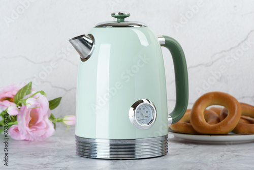 Modern electric kettle on kitchen table with roses and bagels in background. © svdolgov