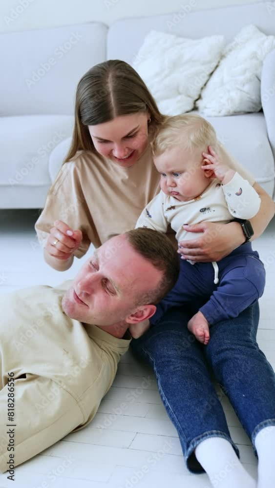 Caucasian family spending time together at home. Woman sits on the floor holding a baby and man lies on her knees. Top view. Vertical video. Caucasian family spending time together at home. Woman sits on the floor holding a baby and man lies on her knees. Top view. Vertical video.